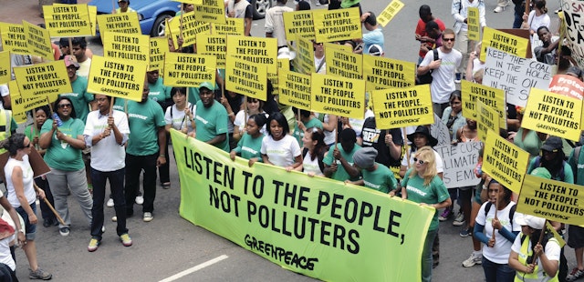 Greenpeace protesters in the street, most have placard and some hold a large banner. The placards and banner all read: 'Listen to the people, not polluters'