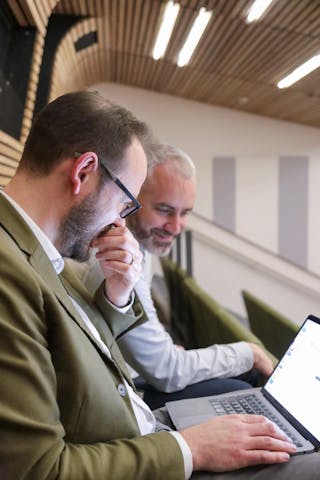 Two men sat in an auditorium looking at a laptop