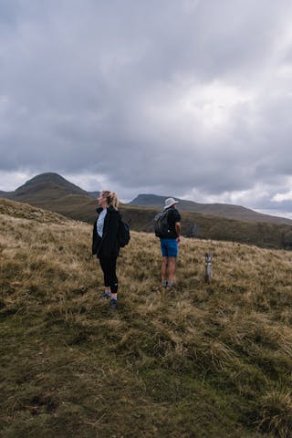 A man and a woman standing in the welsh outdoors, looking in opposite directions