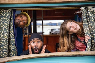 A caravan window, three people popping there heads out at different angles.