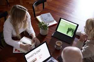 Three people sitting around a wooden table, looking at a tablet and laptop with Backlit Gallery website designs