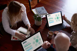 Three people sitting around a wooden table, looking at a tablet and laptop with audience data
