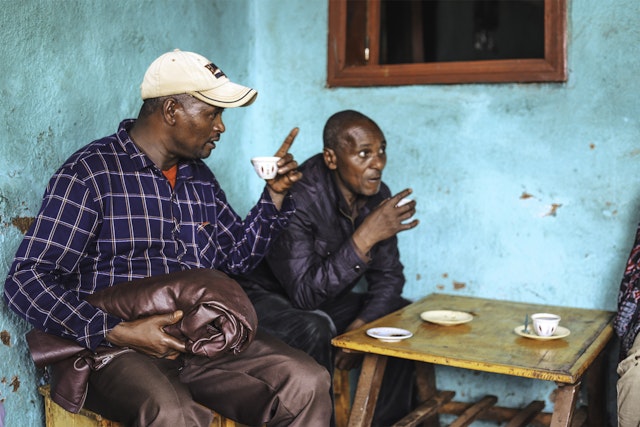 Two men drinking coffee outside a blue building