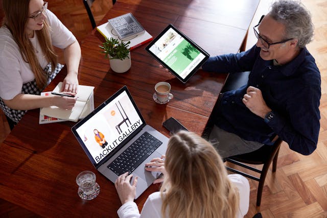 Kind team sat around a table looking at a laptop and an ipad