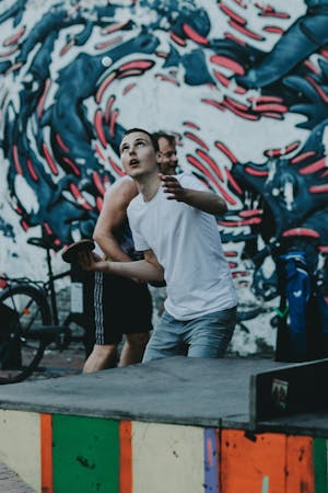 A young man in an urban setting holds a table tennis paddle, he's looking upward as if waiting for a ball to drop