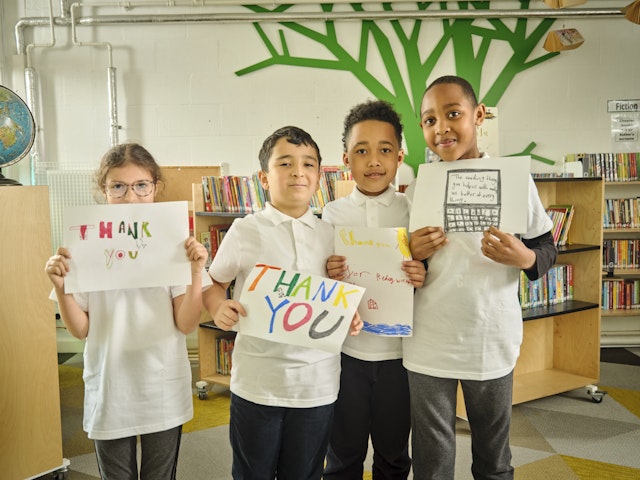 Children in a classroom holding handdrawn 'Thank you' signs