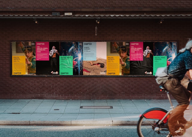 A view of multiple poster mockups lined up on the street. The back end of the bicycle is visible on the right-hand side as it goes past.