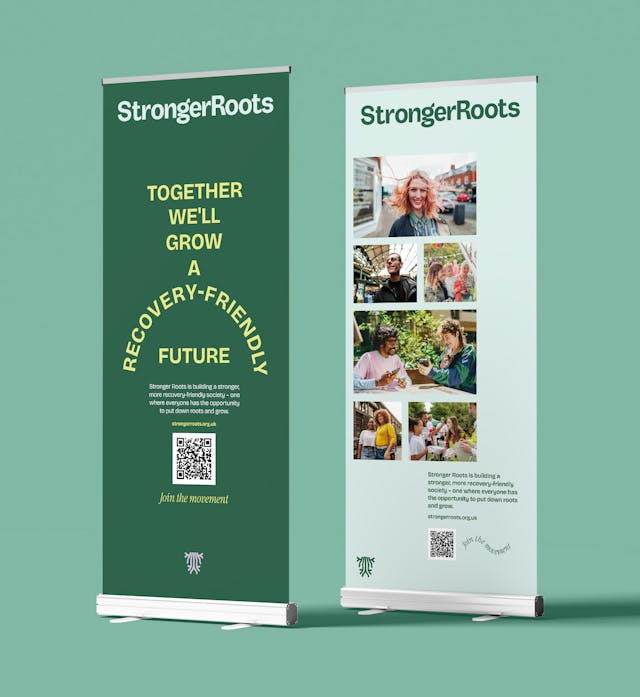Two StrongerRoots pull-up banners displaying campaign messaging, photos of volunteers and the tagline “Together we’ll grow a recovery-friendly future.”