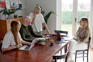 Kind team members meeting around a wooden table with laptops.
