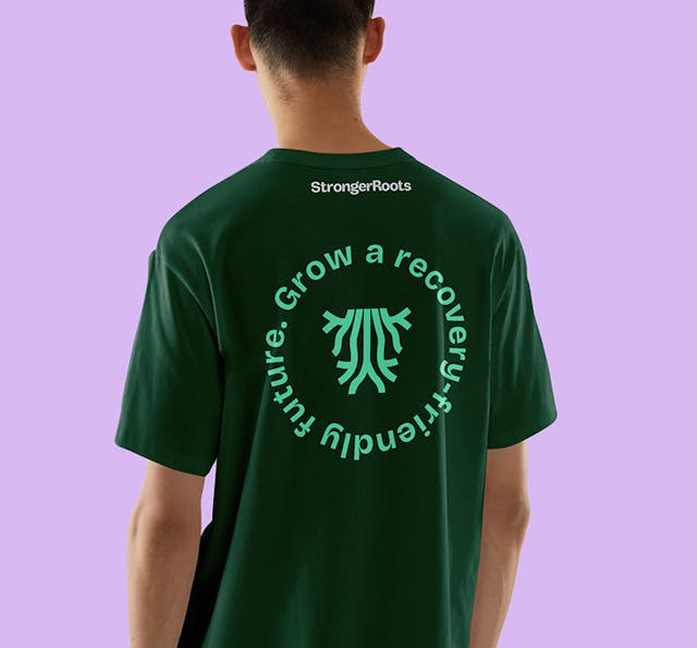 Person wearing a green StrongerRoots T-shirt featuring the circular message “Grow a recovery-friendly future.”