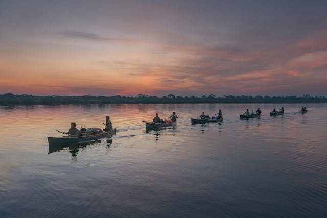 Multiple canoes on a calm river that reflects the colorful sunset sky.