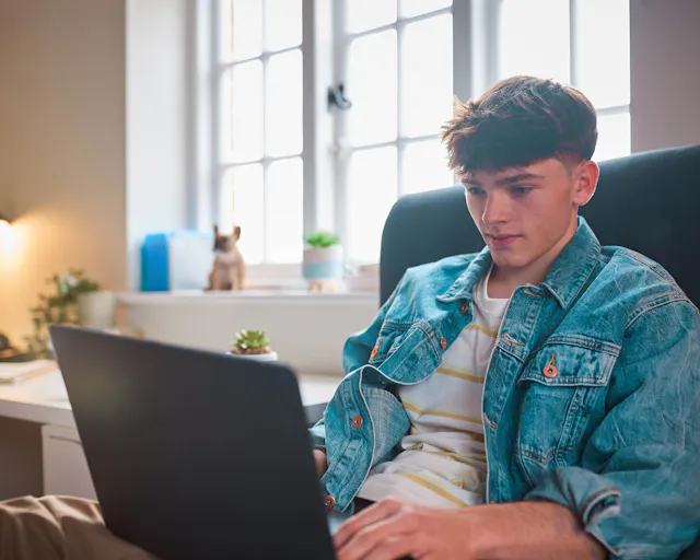 A young man sat in a chair with a laptop