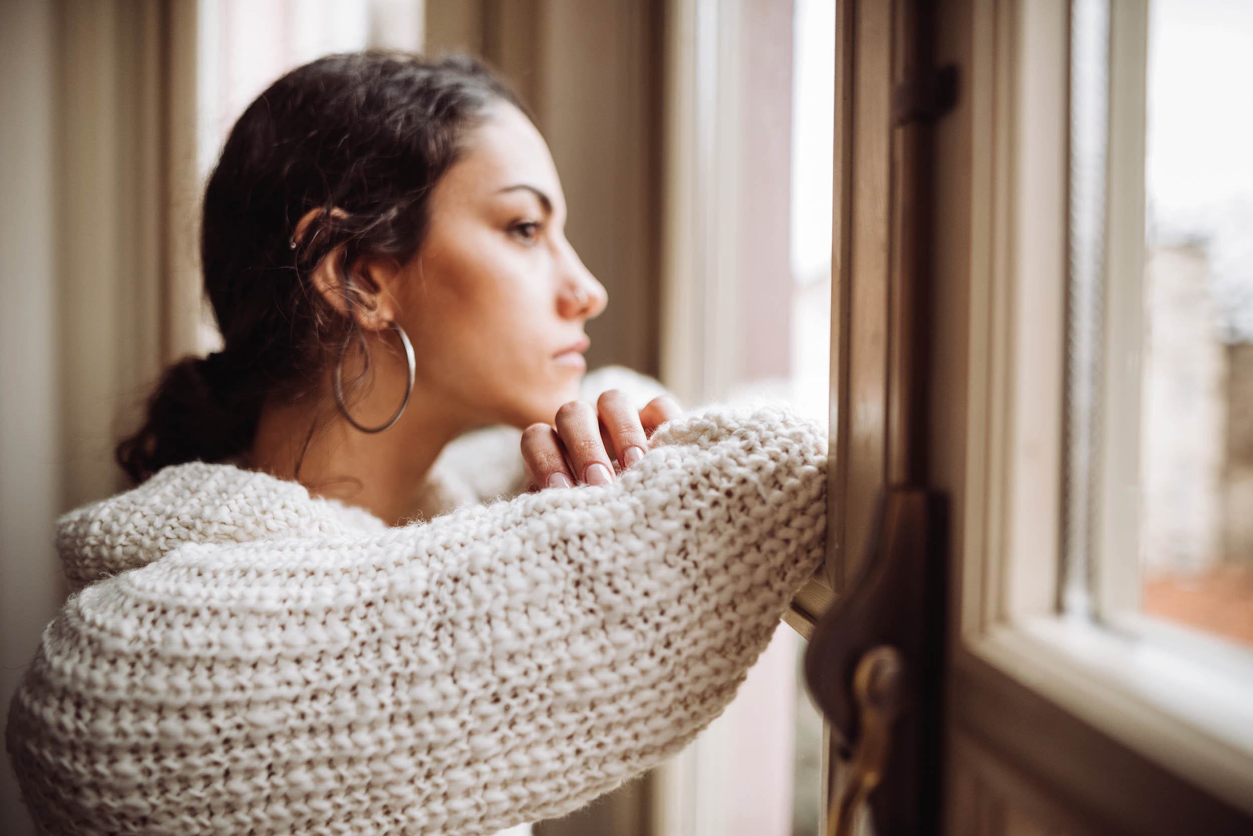 A young woman looks out of the window, wearing a knitted white jumper