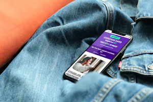 A mobile phone on a denim jacket. The mobile phone has the Papyrus website on the screen